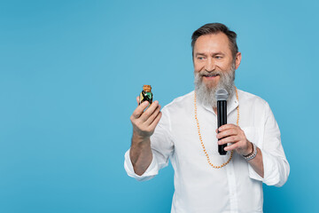 smiling ayurveda guru with bottle of essential oil talking in microphone isolated on blue.