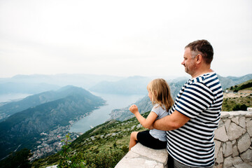 Dad and daughter in common family look stand on the view point and look at the Kotor Bay in Monenegro. Traveling family concept.