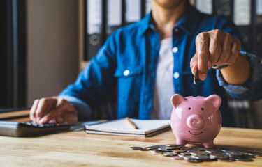 woman holds a coin in a pig-shaped piggy bank to save money for the future. after retirement and...