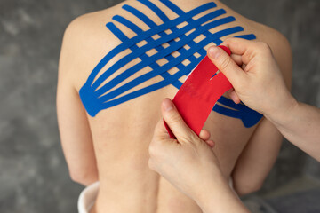 Closeup cropped doctor, physiotherapist hands taping blue, red stripes on back muscles for kinesiology therapy treatment - obrazy, fototapety, plakaty