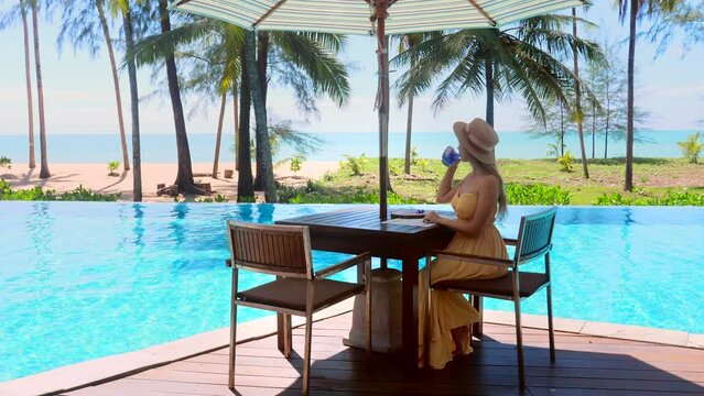 Young travel woman celebrating summer vacation. Female traveler relaxing in poolside cafe at luxury exotic hotel resort, enjoy beautiful sea view of mediterranean travel holiday.