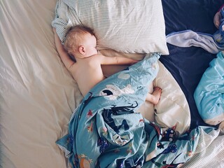 Adorable and cute 12 month or one year old baby boy taking a nap. Toddler lying on the bed. Baby sleeping routine.