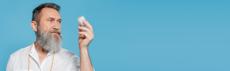 senior spiritual guru meditating with selenite stone isolated on blue, banner.
