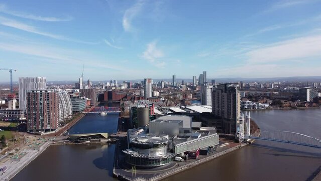Aerial footage of modern buildings surrounded by water with Manchester skyline in  the background. Drone video Salford Quays England. 
