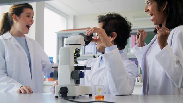 science research, work and people concept - international team of scientists with microscope working in laboratory and making high five gesture