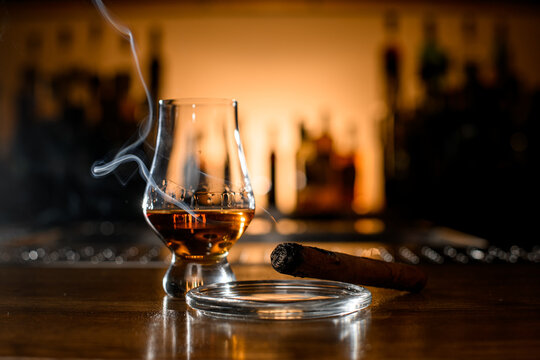 Close-up of smoking cigar and glass with whiskey on blurred bar background