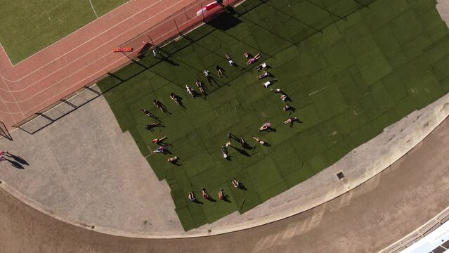 Kids doing situps by running track, top down rotating aerial