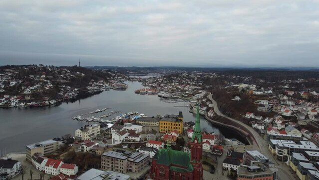 Arendal Norway - Flying above city center with trinity church and Tyvholmen while looking west towards Stromsbu and Bie - Cloudy morning aerial
