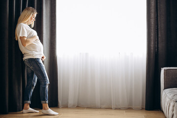 Pregnant woman hugging her belly by the window at home