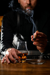 smoking cigar in the hand of a male bartender and a glass of cognac