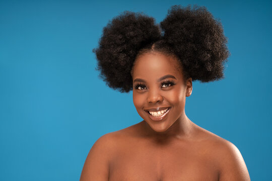 Beauty portrait of african young woman with clean healthy skin smiling and looking to the camera, posing on blue studio background.