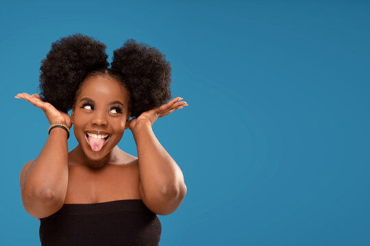 Funny dark-skinned young afro woman sticking tongue and making faces to the camera. Real people emotions.
