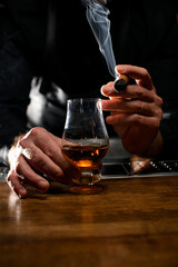 Glass of cognac on bar counter and smoking cigar in male hand