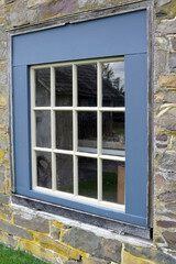 A rustic, square, multi-paned window grid with colonial blue painted-wood trim set in a stone wall