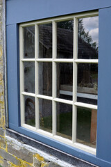 A rustic, square, multi-paned window grid with colonial blue painted-wood trim set in a stone wall