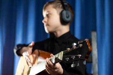 A thirteen-year-old teenager in a black shirt and headphones with a guitar in a music studio...