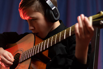 A thirteen-year-old teenager in a black shirt and headphones with a guitar in a music studio...
