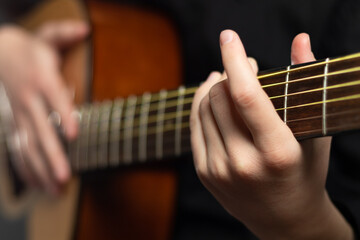 Fototapeta na wymiar The hands of a young musician playing an acoustic guitar with metal strings close-up with a blurred background. selective focus