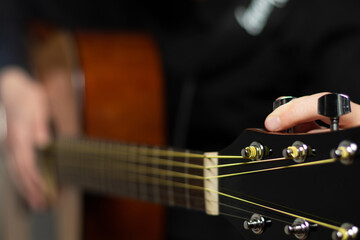 The hands of a young musician playing an acoustic guitar with metal strings close-up with a blurred...