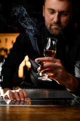 selective focus on male hand holding glass of cognac and smoking cuban cigar