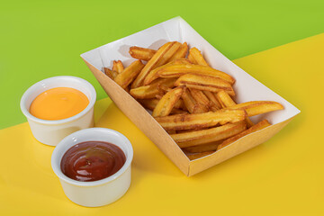 French fries with two sauces in a paper plate. Fast food. Colored background.