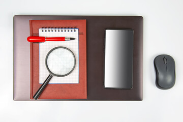 Laptop, magnifying glass, computer mouse, smartphone, pen, notepad on a white background. Items for business and buying goods online