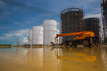 Constuction of an oil derrick crane, big oil tanks water background