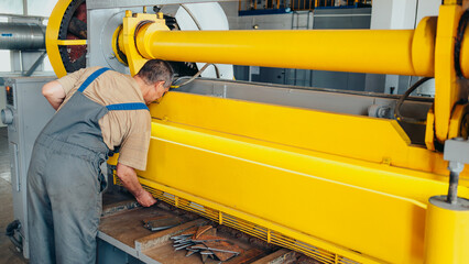 Worker cuts metal sheets on mechanical guillotine machine in production hall. Industrial equipment...