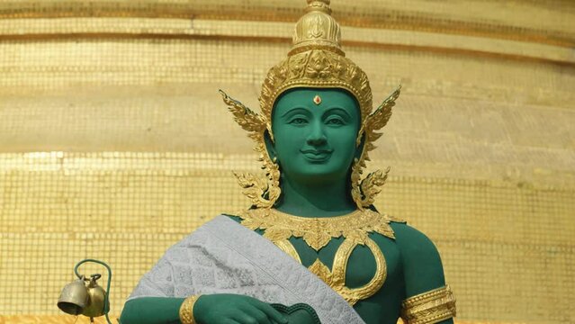 4K Cinematic slow motion footage of a golden and green statue of a Buddhist religious entity figure on top of the Golden Mount Temple in Bangkok, Thailand on a sunny day.