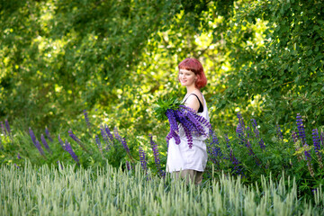 Fototapeta premium A cute teenage girl with pink hair and a bouquet of lupines is standing in a yellow raincoat