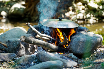 flames burning the pot, hearth with the pot on the river bank, picnic in the woods