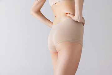 Cropped image of female body, buttocks in beige underwear isolated over grey studio background. Anti-cellulite care.