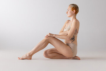 Side view portrait of young short-haired woman posing in underwear isolated over grey studio background. Well-being