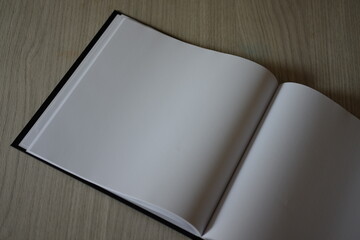 Skatebook, black cover, white paper, placed on a wooden table.
