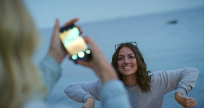 Friends having fun on the beach with a sparkler. A woman taking a photo of her friend with a smartphone playing with a sparkler on the beach