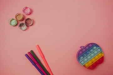 Colorful antistress sensory toy fidget push pop it, paints and markers on pink background. Copy space for design