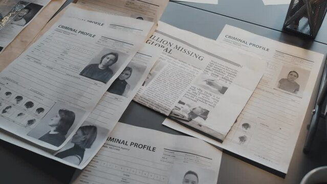 Criminal profiles of diverse offenders with pictures and fingerprints, newspaper at desk in office at daytime