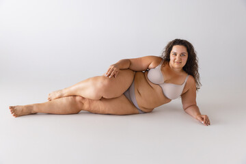 Portrait of beautiful woman with plum figure posing in underwear isolated over grey studio background. Self-acceptance, self-love