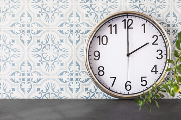Fototapeta na wymiar Classic, round wall clock on a marble shelf on a tile wall with home plant. Part of interior with big wall chrome clock showing 2 hours and empty space