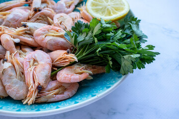 Сooked shrimp with parsley and lemon in a blue ceramic bowl on a white marble table background. Healthy Mediterranean seafood. Top view, flat lay, copy space