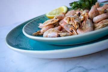 Сooked shrimp with parsley and lemon in a blue ceramic bowl on a white marble table background. Healthy Mediterranean seafood. Top view, flat lay, copy space