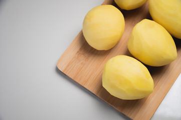 Peeled fresh potatoes lie on a wooden cutting board on a white table