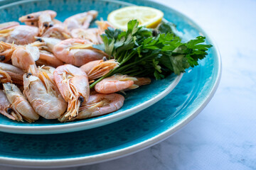 Сooked shrimp with parsley and lemon in a blue ceramic bowl on a white marble table background. Healthy Mediterranean seafood. Top view, flat lay, copy space