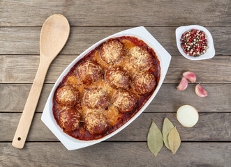 Meat balls on a white plate with tomato sauce, melted cheese and seasonings