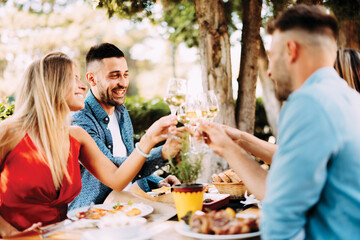 Group of young happy people toast with wine at lunch in restaurant during a sunny summer day