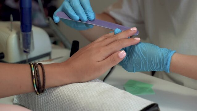 Professional manicure master with gloves ais polishing nails using file, during the manicure procedure. Small business in covid 19 pandemic. close up view. 4k footage