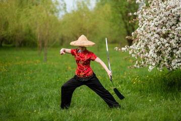 Asian woman with sword training with tai chi in the park, chinese martial arts, healthy lifestyle...