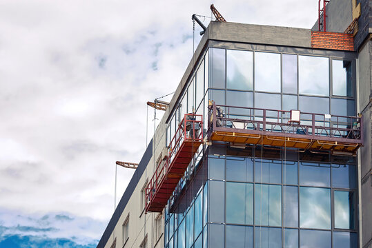 Suspended platform, construction craddle hanging on building. Installation and repair work. Building facades construction works. Glass facade of high-rise building under construction, finishing works