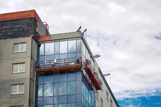 Suspended platform, construction craddle hanging on building. Installation and repair works. Building facades construction works. Glass facade of high-rise building under construction