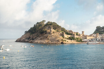 view of the beach and the castle of tossa de mar in a summer day with clouds, catalonia, spain